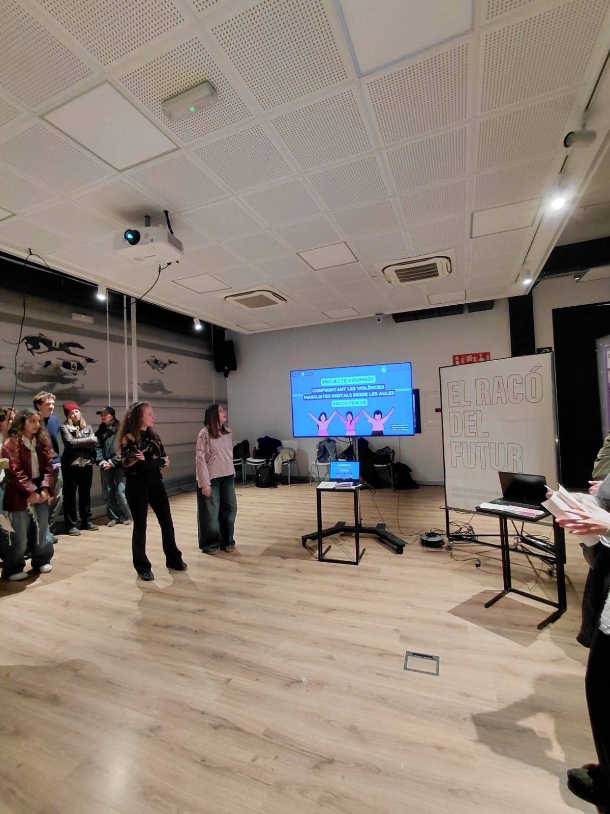 Moment d’una intervenció durant la sessió, amb participants davant la pantalla de materials.